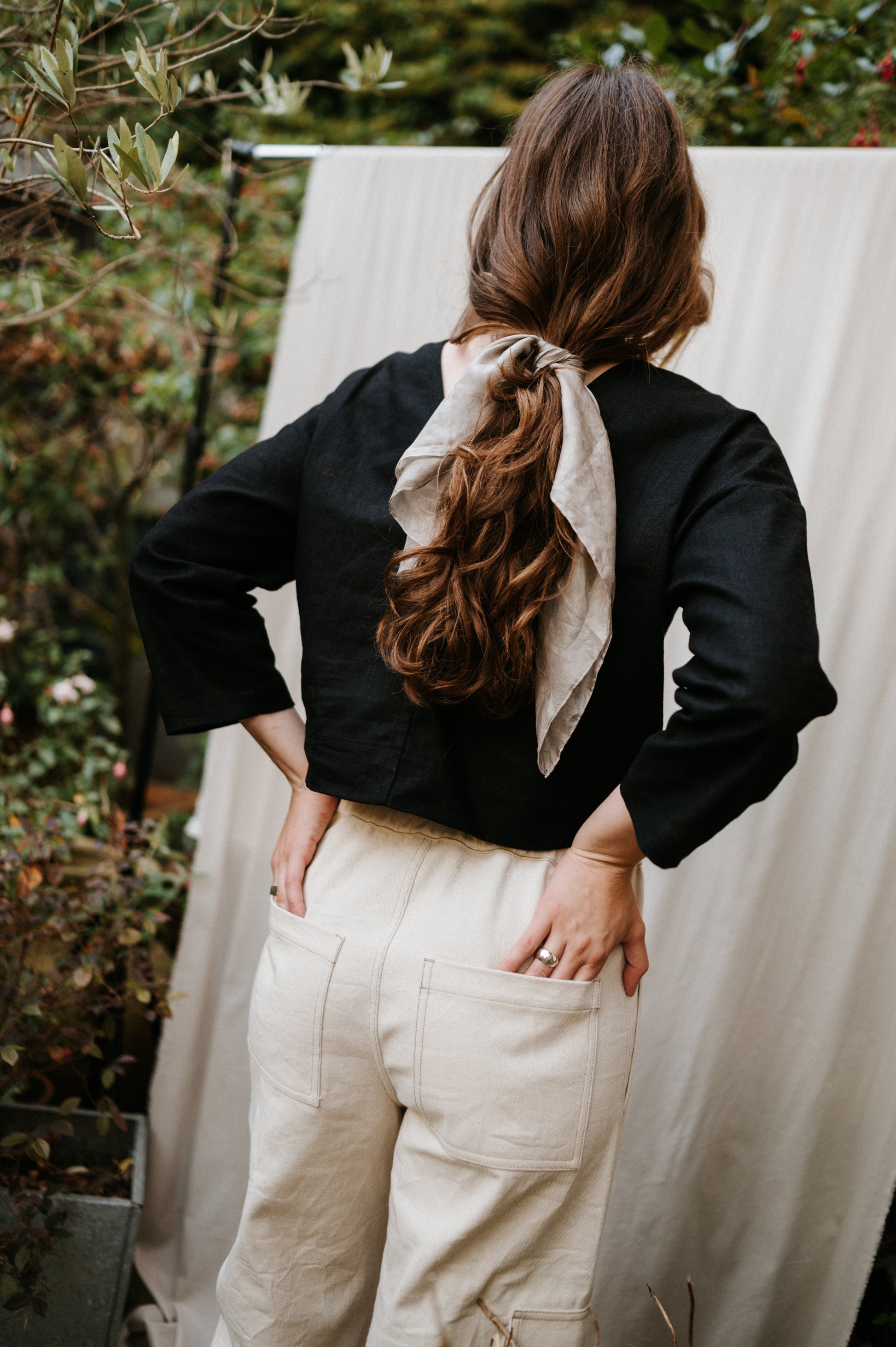 Person wearing a black top and beige pants with a scarf, standing outdoors.