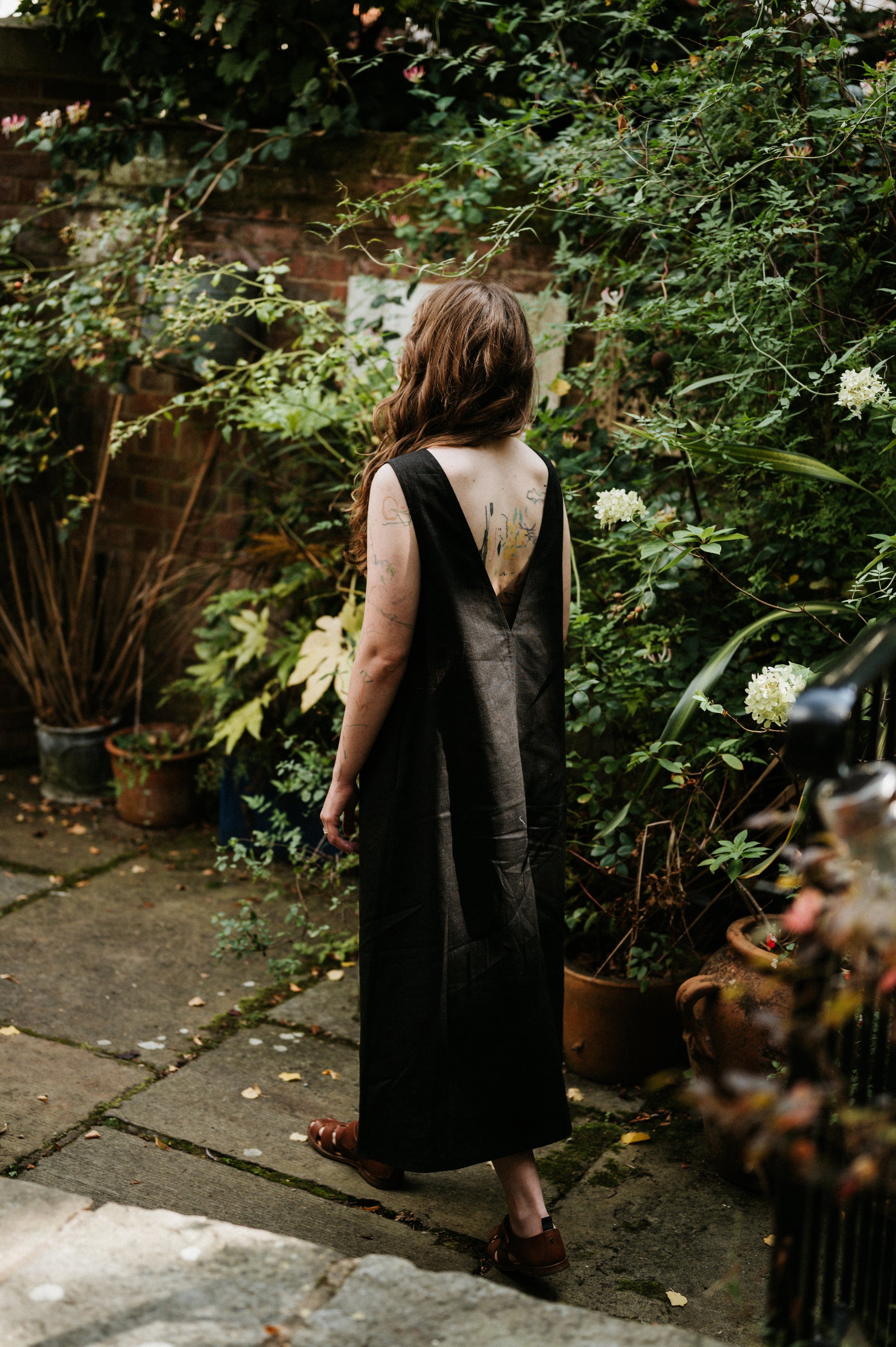 woman standing with her back to us in a low back black linen dress in a garden setting