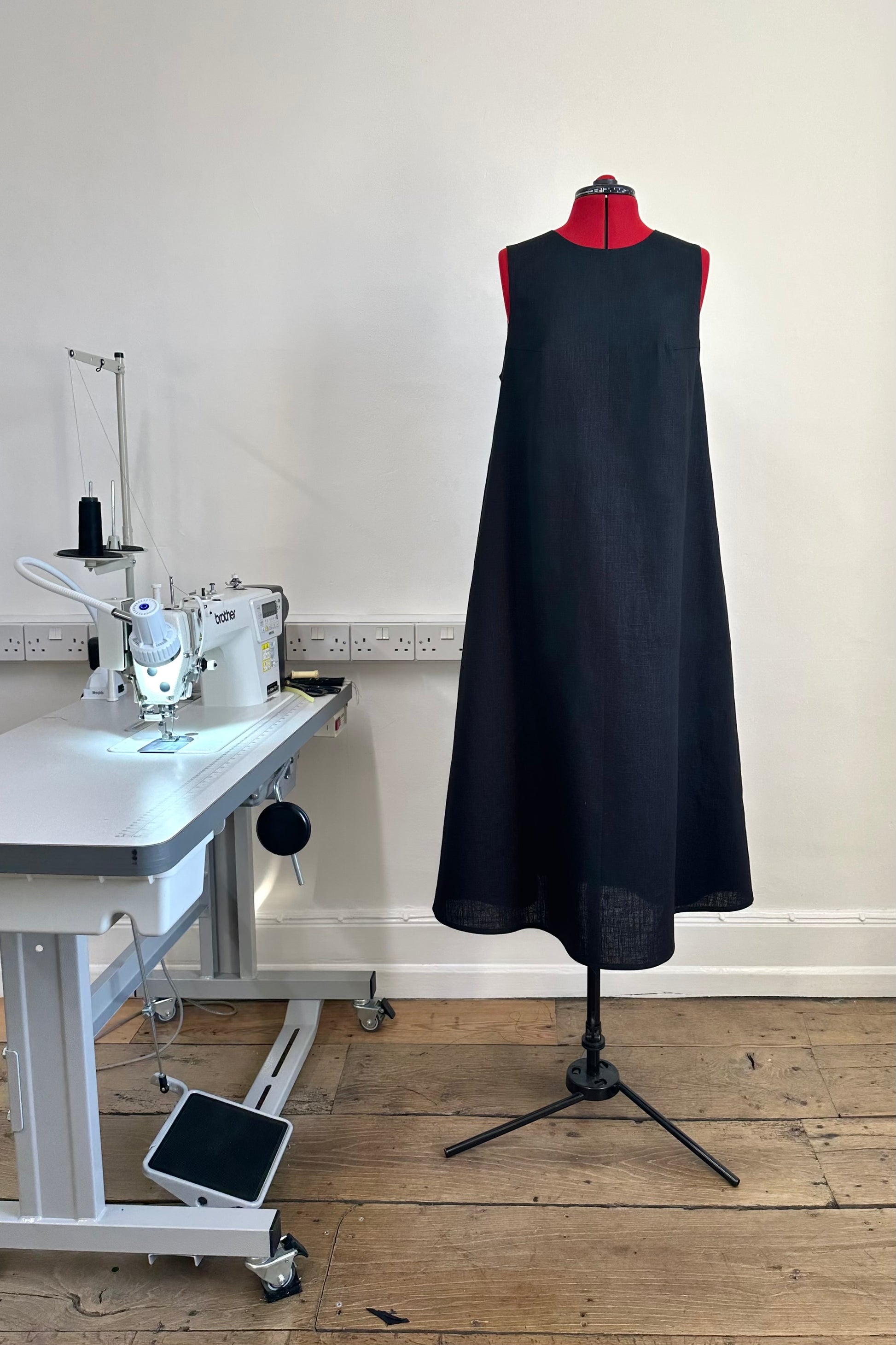 A black sleeveless, high neck dress with a deep v-back on a mannequin in a sewing studio setting, indicating a fitted garment made from ramie linen.