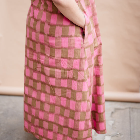 Person wearing a pink and brown checkered dress standing on a concrete floor.