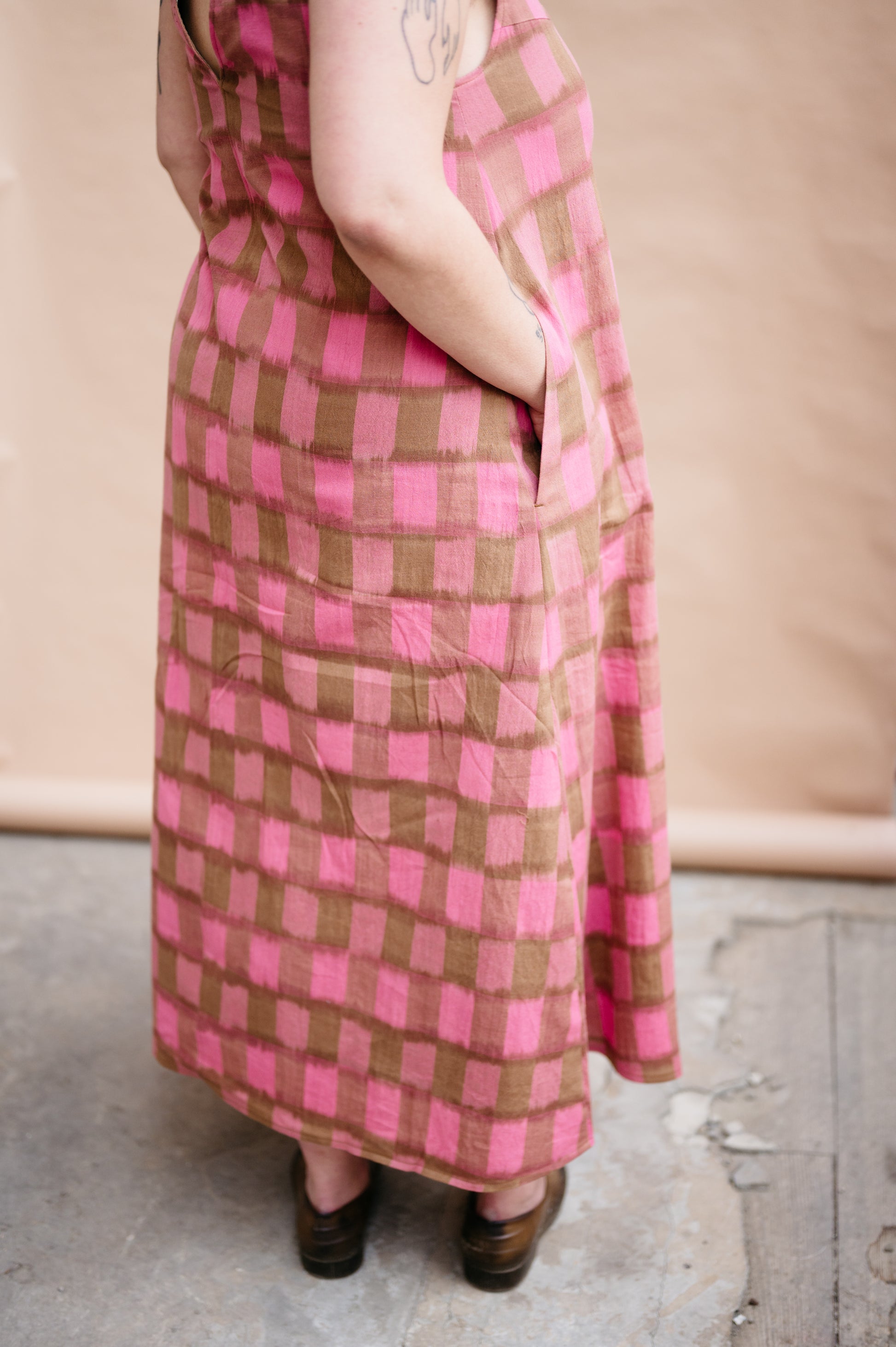 Person wearing a pink and brown checkered dress standing on a concrete floor.