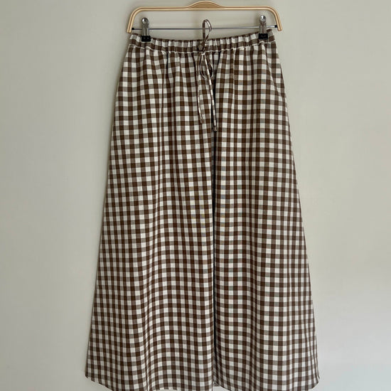 A brown cotton gingham skirt with a drawstring waist, displayed on a hanger against a white background.