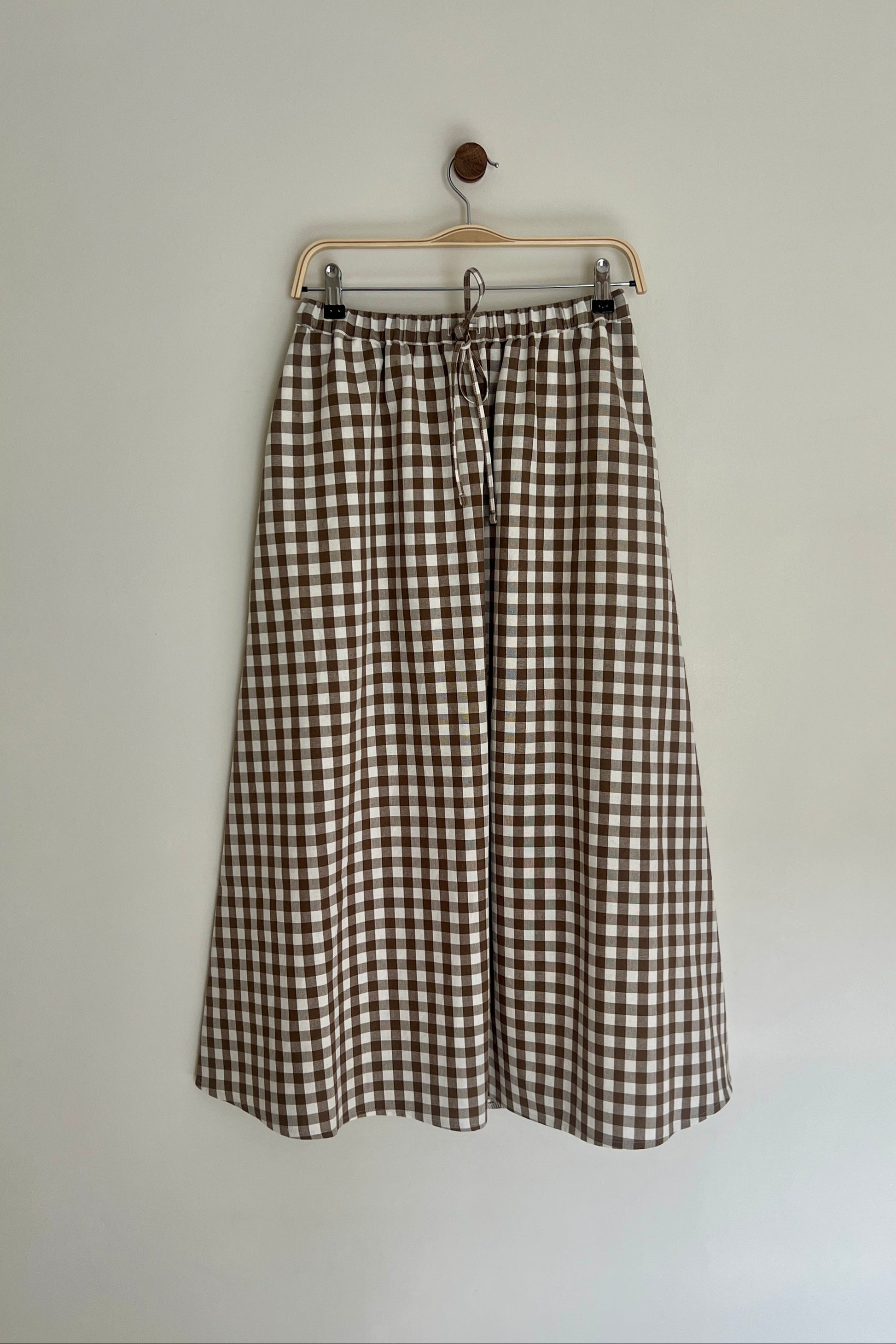 A brown cotton gingham skirt with a drawstring waist, displayed on a hanger against a white background.
