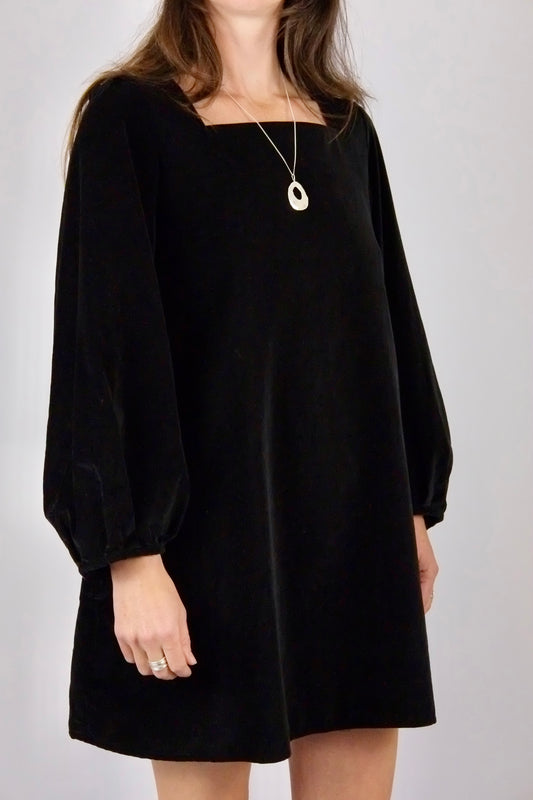 Person wearing a black velvet mini dress handmade by atwin the label with long sleeves on a plain background