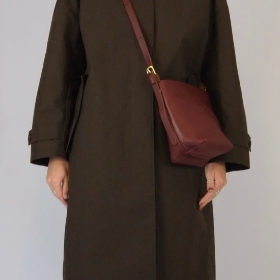 Person wearing a brown coat with a maroon bag on a plain background