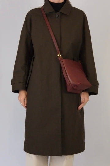Person wearing a brown coat with a maroon bag on a plain background