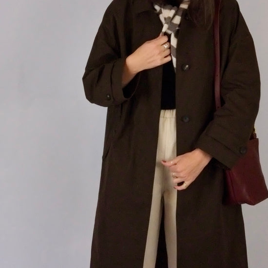 Woman wearing a brown coat holding a red bag against a plain background