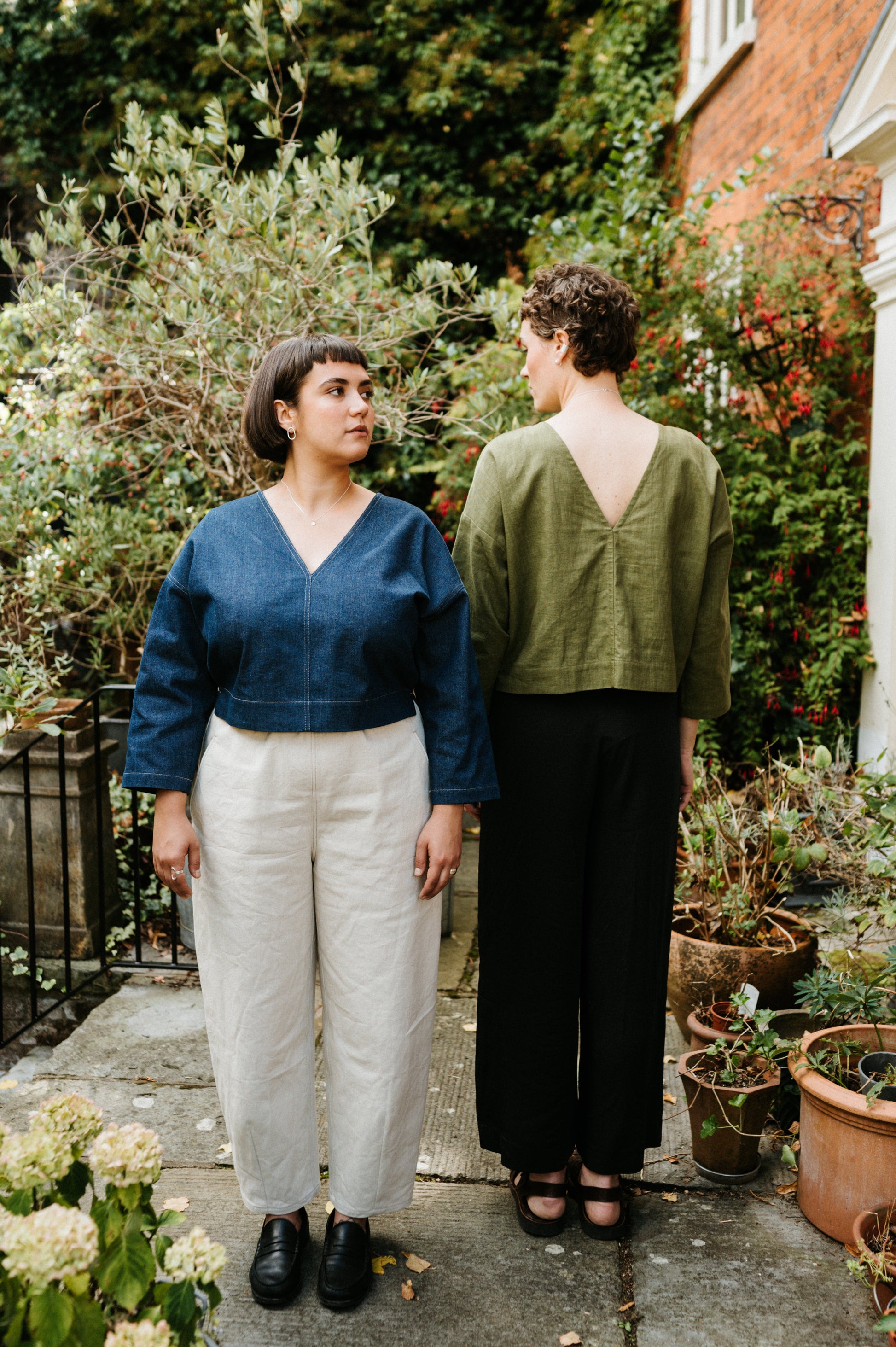 Two women standing in a garden with plants and flowers around them.