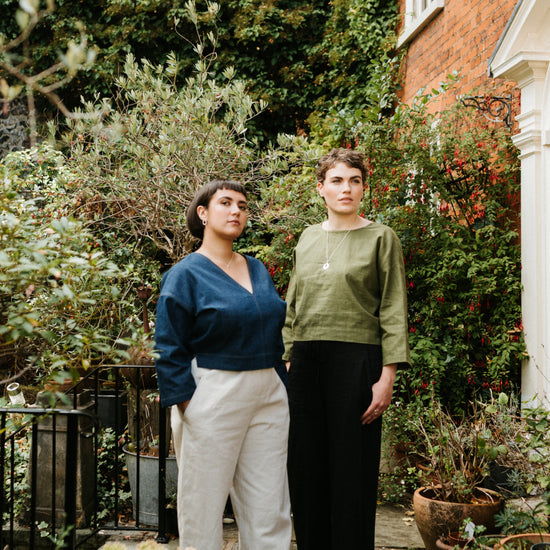 Two women standing in a garden with greenery and a house in the background