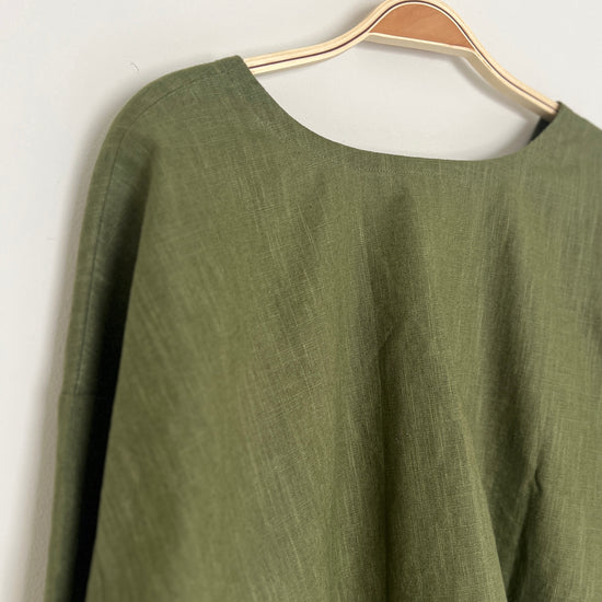 khaki linen top on a hanger against a white wall