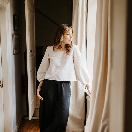 Woman standing in a room with white curtains and a rug.