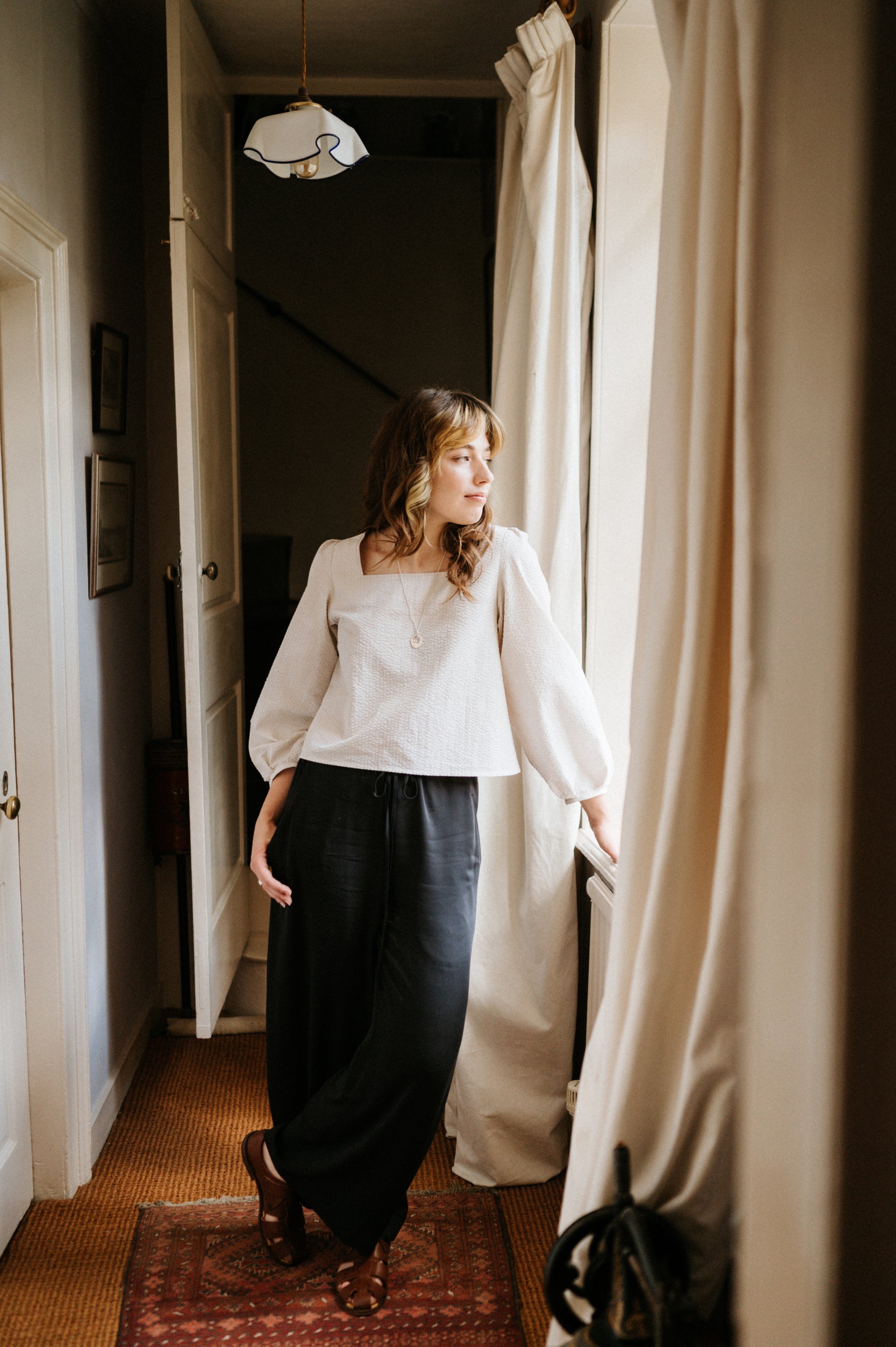 Woman standing in a room with white curtains and a rug.
