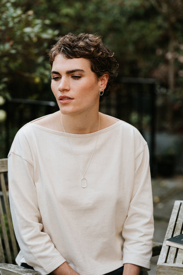 Woman wearing a white smock sweater sitting outdoors with a blurred background