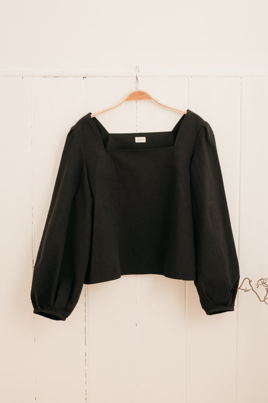 handmade seersucker blouse in black hanging on a hook against a wall