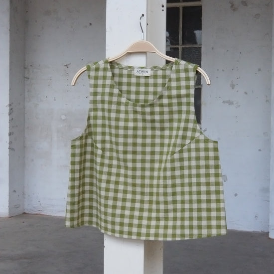 Green checkered vest top on a hanger against a concrete wall.