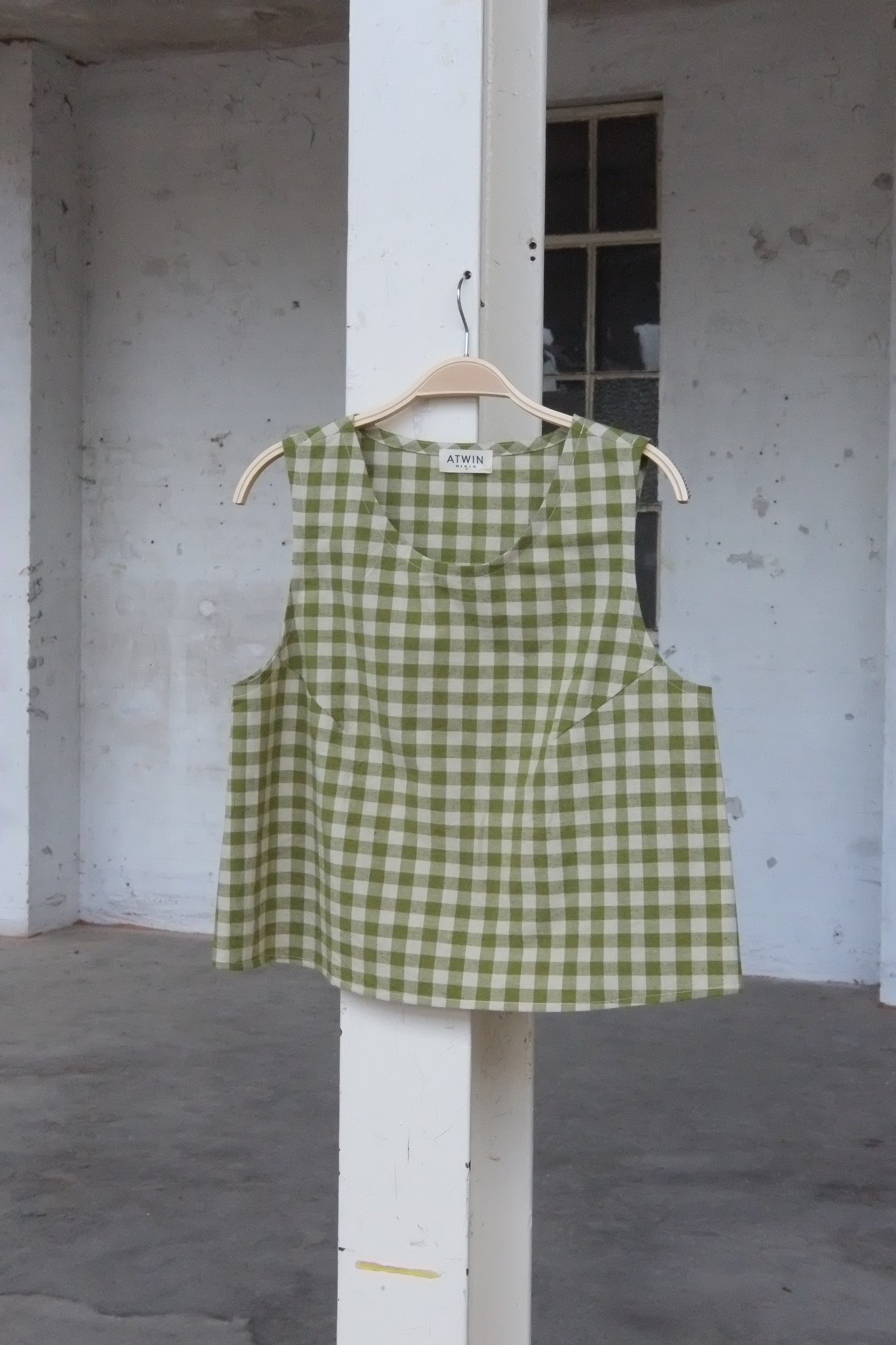Green checkered vest top on a hanger against a concrete wall.