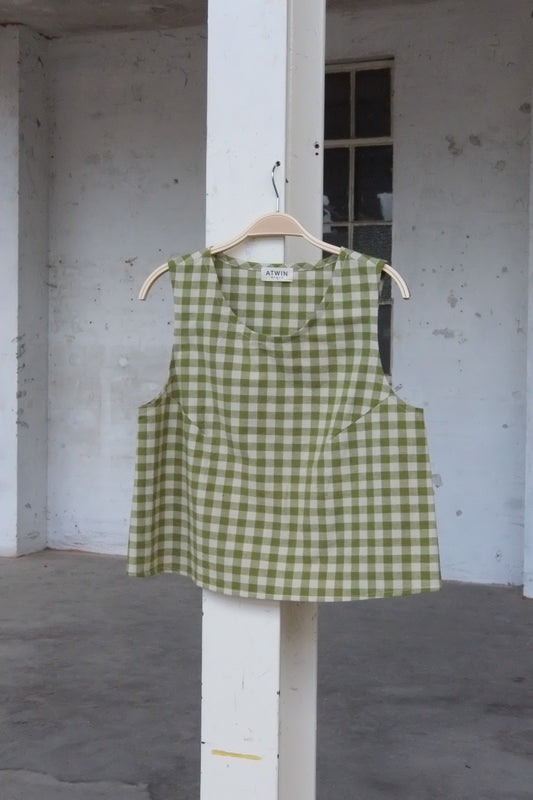 Green checkered vest top on a hanger against a concrete wall.