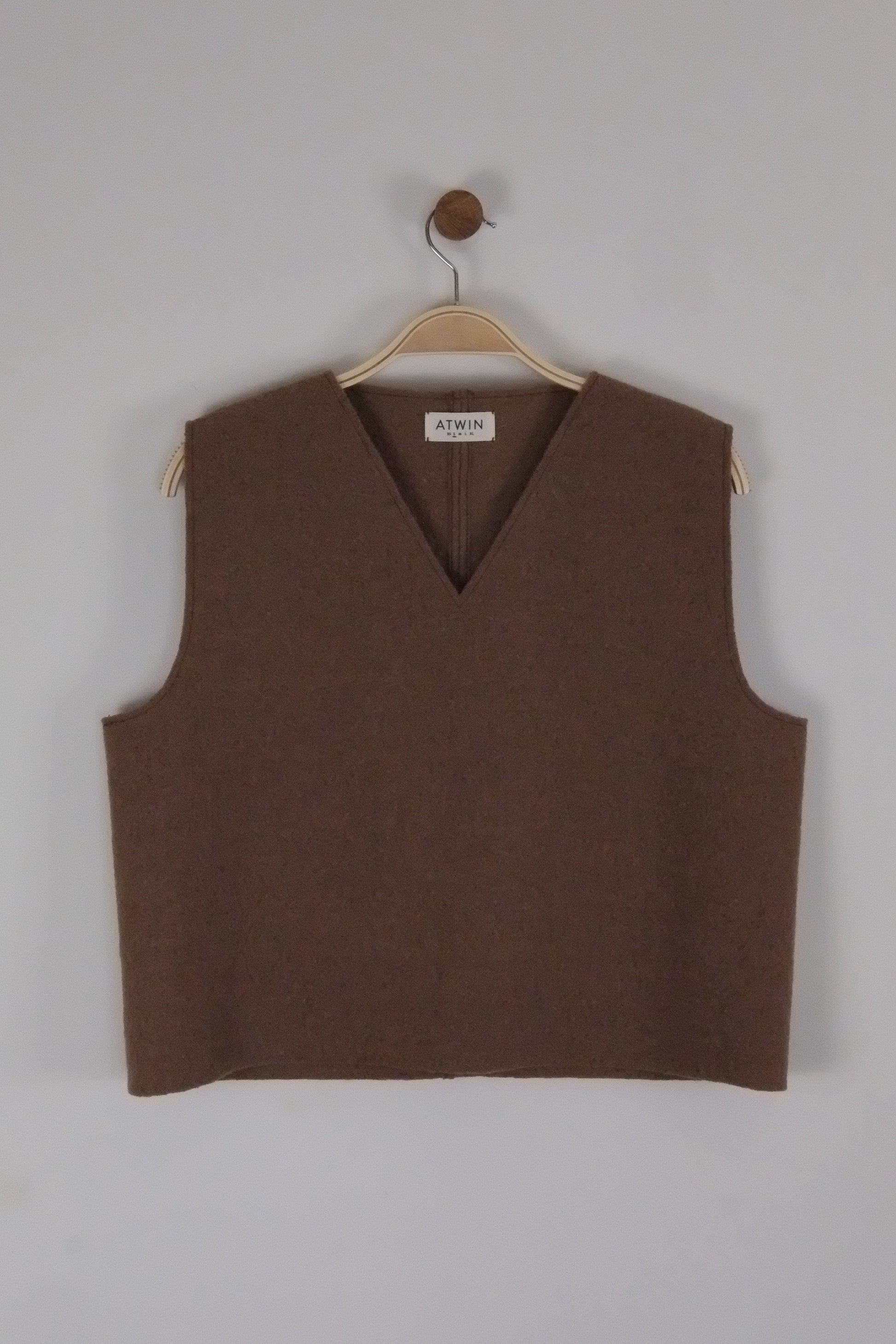 Brown boiled wool vest on a hanger against a light grey background