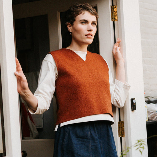Woman standing at the door of a small building with plants around