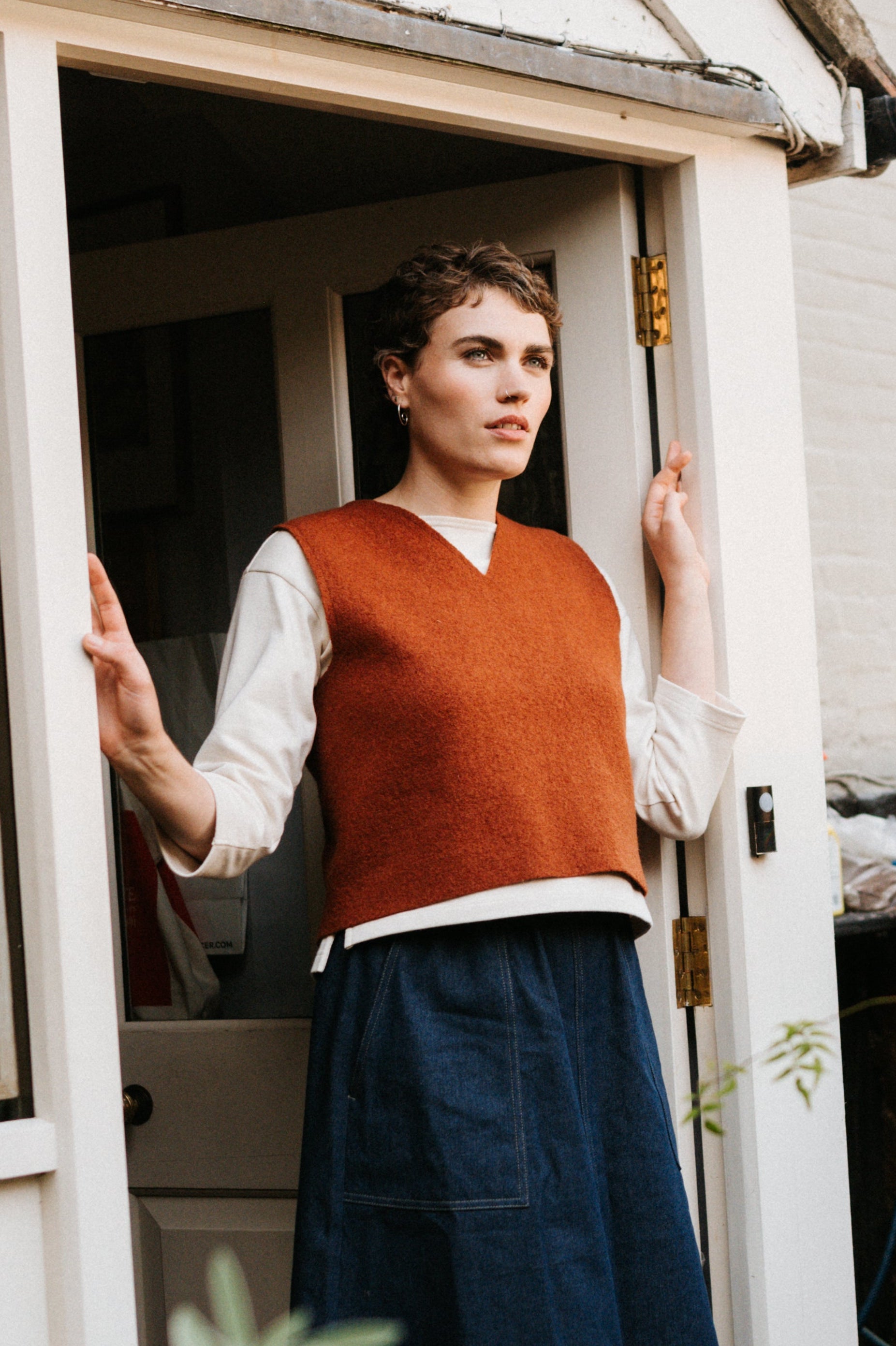 Woman standing at the door of a small building with plants around