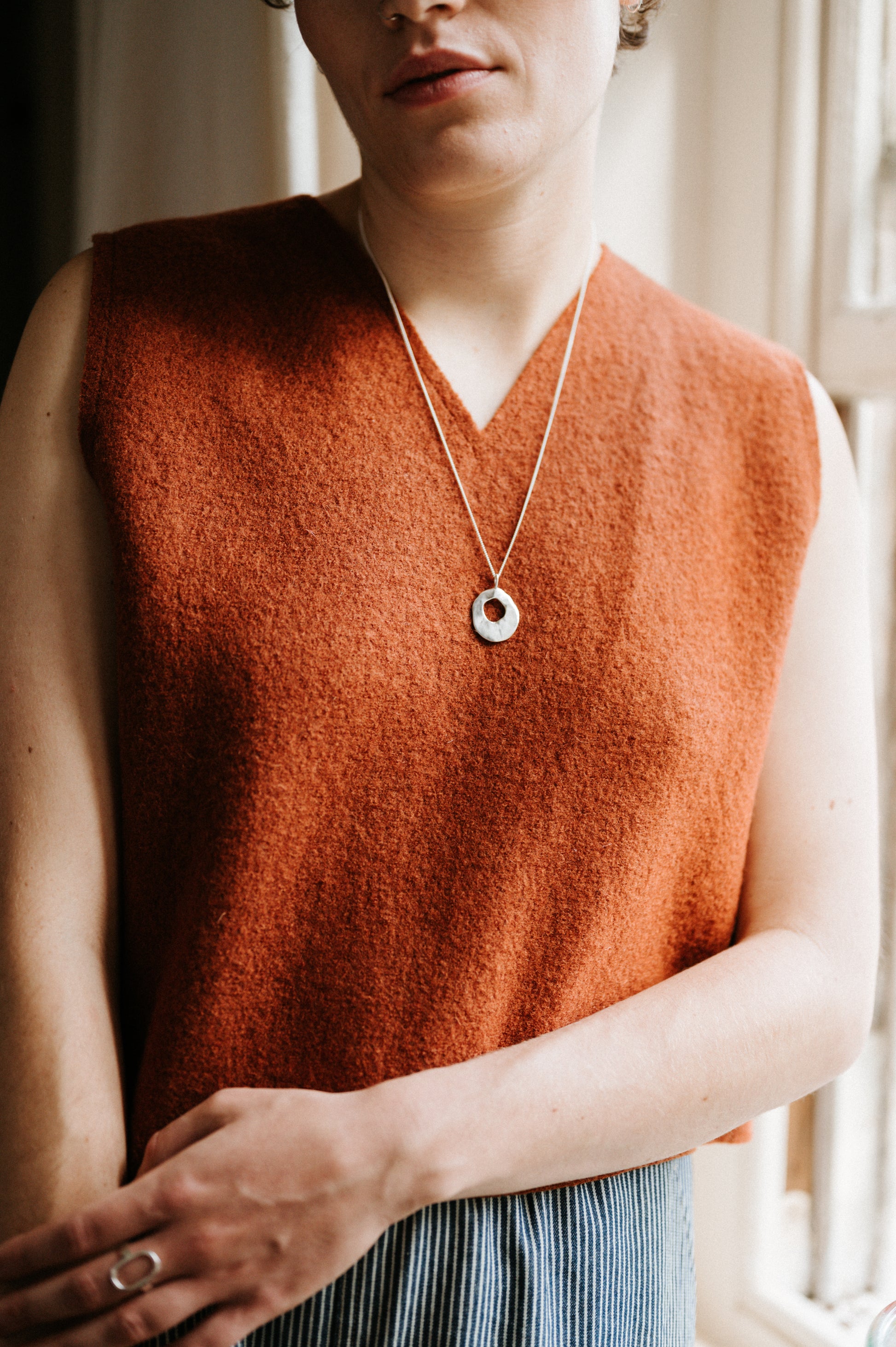 Person wearing a rust-colored sleeveless vest with a necklace, standing indoors.