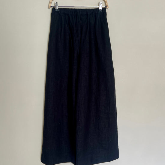 A pair of high-waisted, wide leg trousers in a paprika color, made from linen, displayed on a hanger against a neutral background.