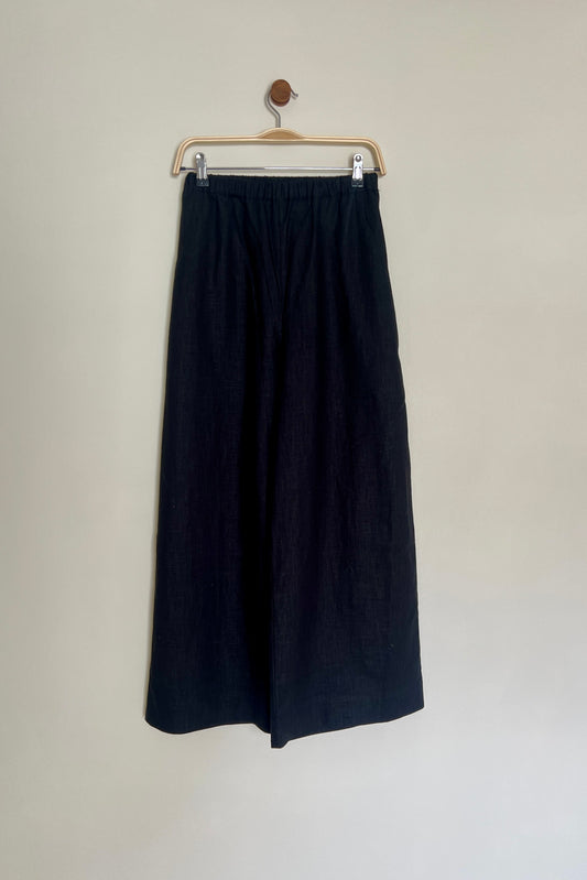 A pair of high-waisted, wide leg trousers in a paprika color, made from linen, displayed on a hanger against a neutral background.