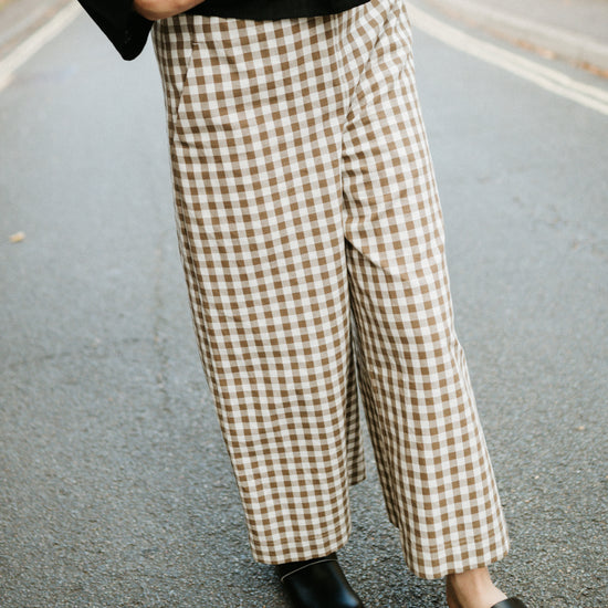 Person wearing checkered wide leg trousers and black shoes on a street.