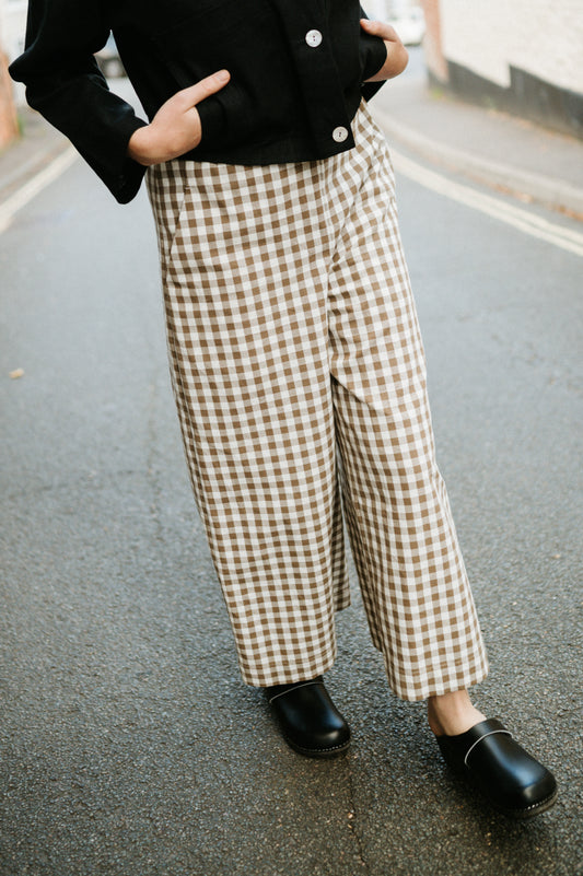 Person wearing checkered wide leg trousers and black shoes on a street.