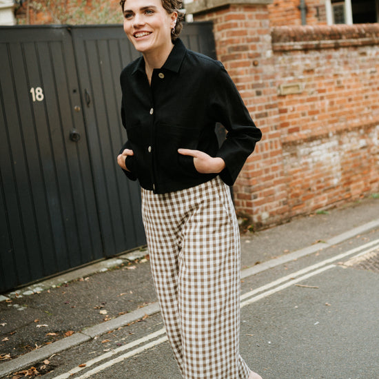 woman walking down the road wearing black jacket and brown gingham wide leg trousers