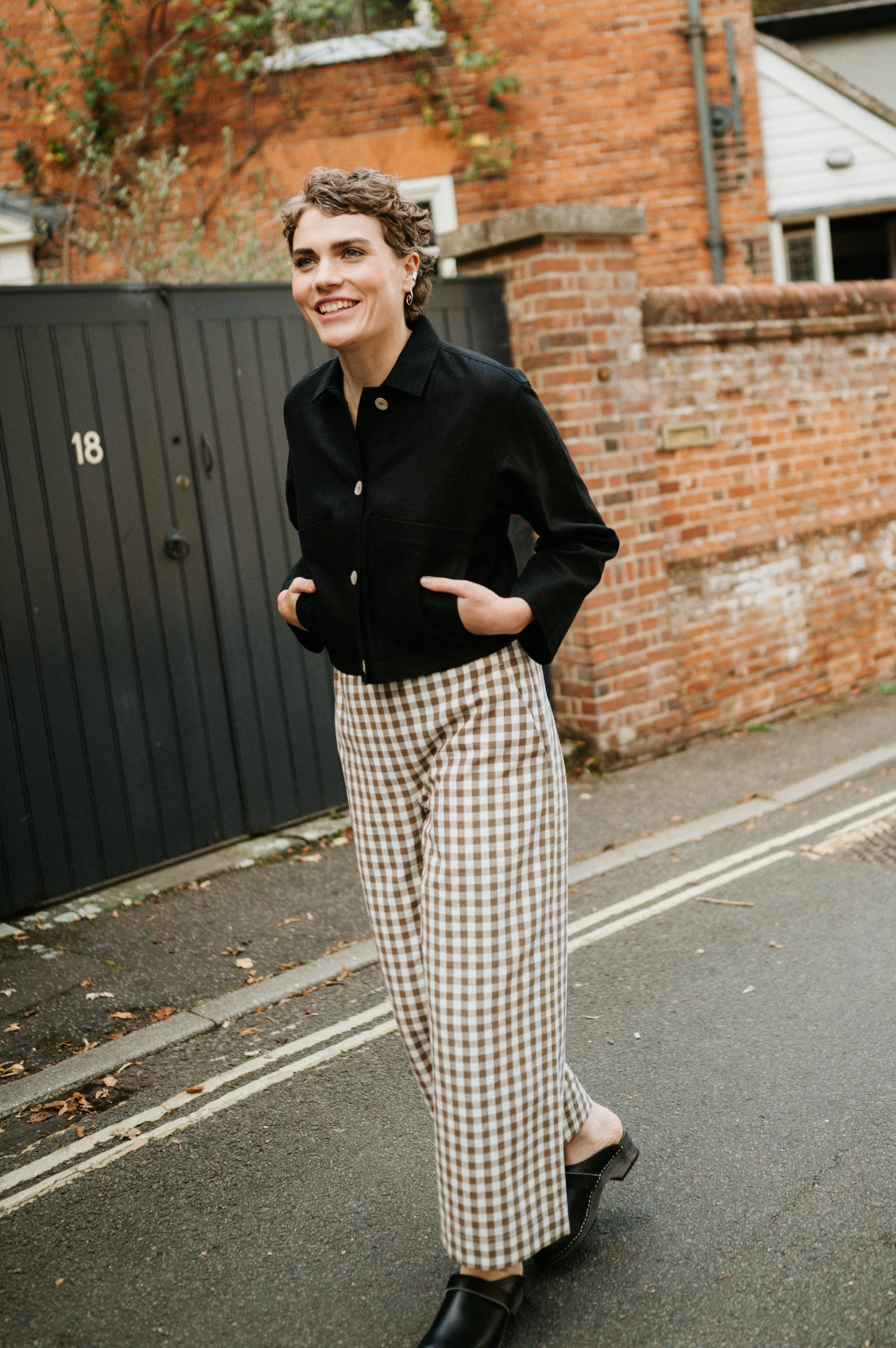 woman walking down the road wearing black jacket and brown gingham wide leg trousers