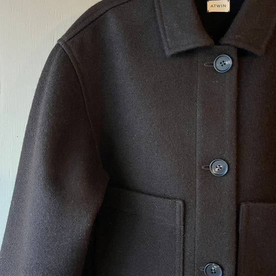 Close-up of a dark brown wool coat with brown buttons, collar and front pockets on a light background