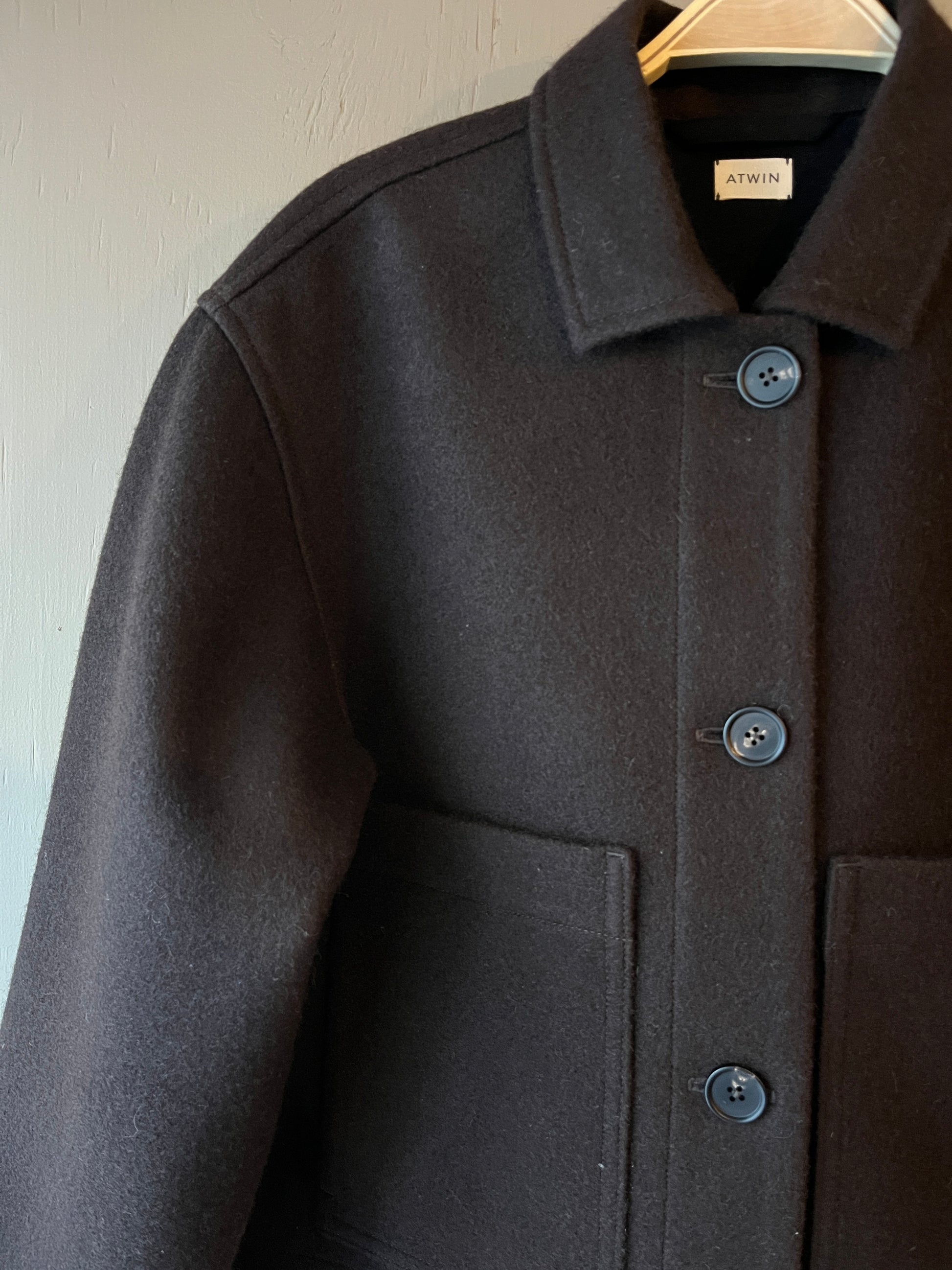 Close-up of a dark brown wool coat with brown buttons, collar and front pockets on a light background