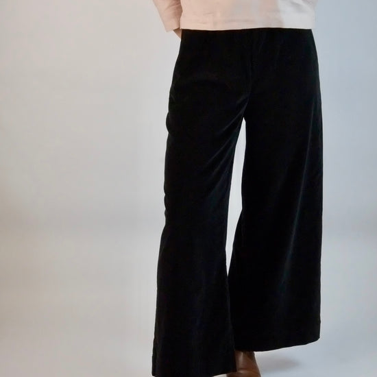 Person wearing black velvet  wide-leg trousers and brown shoes on a white background