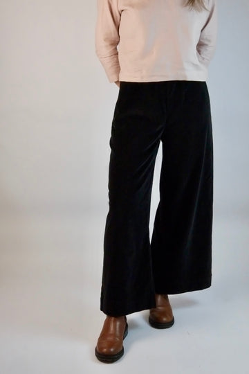 Person wearing black velvet  wide-leg trousers and brown shoes on a white background