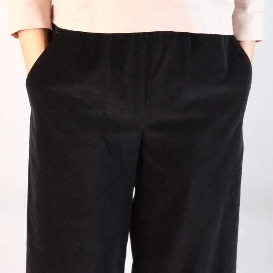 Person wearing black velvet trousers on a plain background