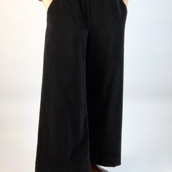 Person wearing black wide-leg velvet trousers on a white background