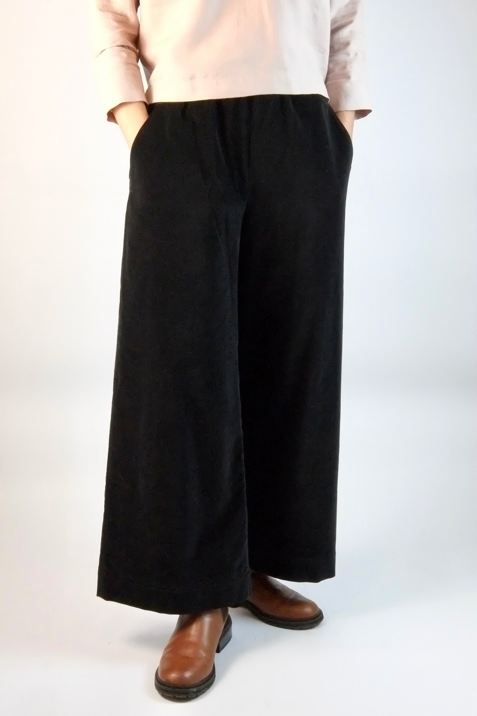 Person wearing black wide-leg velvet trousers on a white background