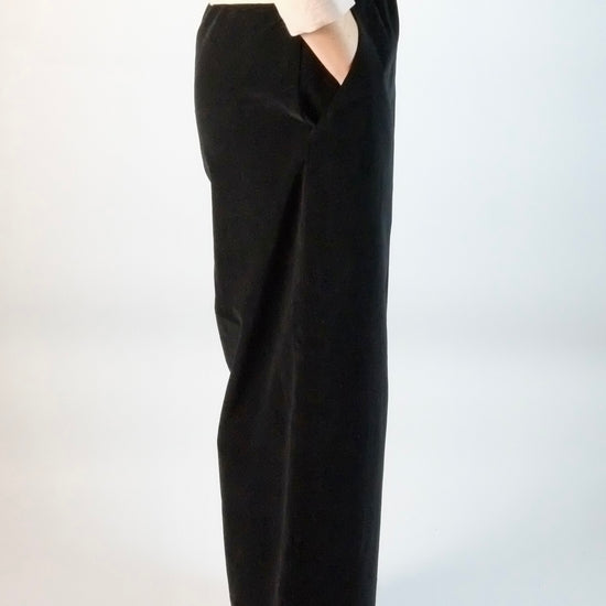Person wearing black wide-leg velvet trousers and a white top on a white background