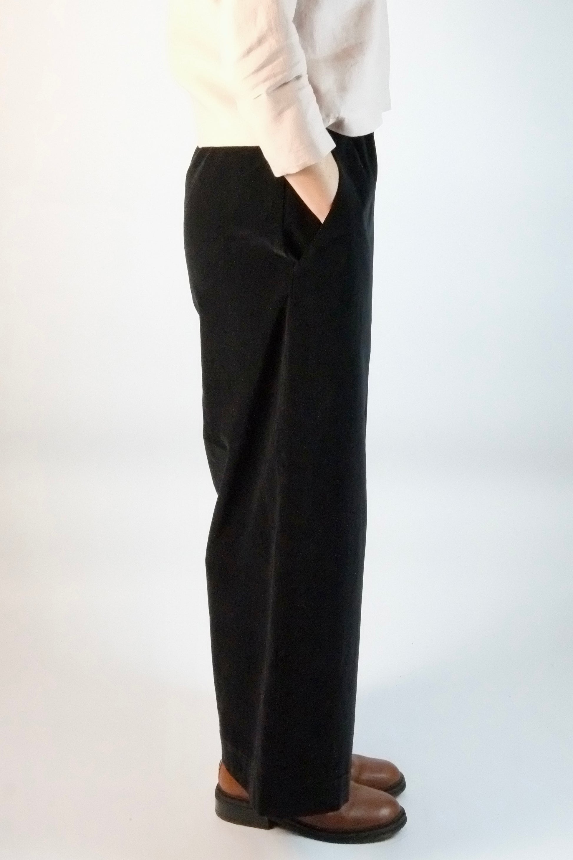 Person wearing black wide-leg velvet trousers and a white top on a white background