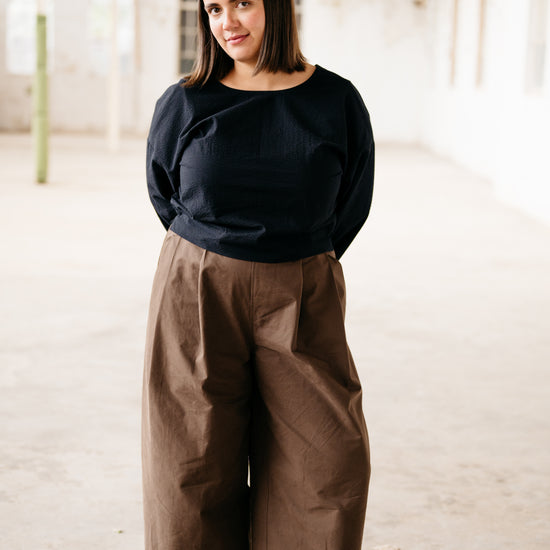 Person wearing a black top and brown pants in an indoor setting with red structural elements.