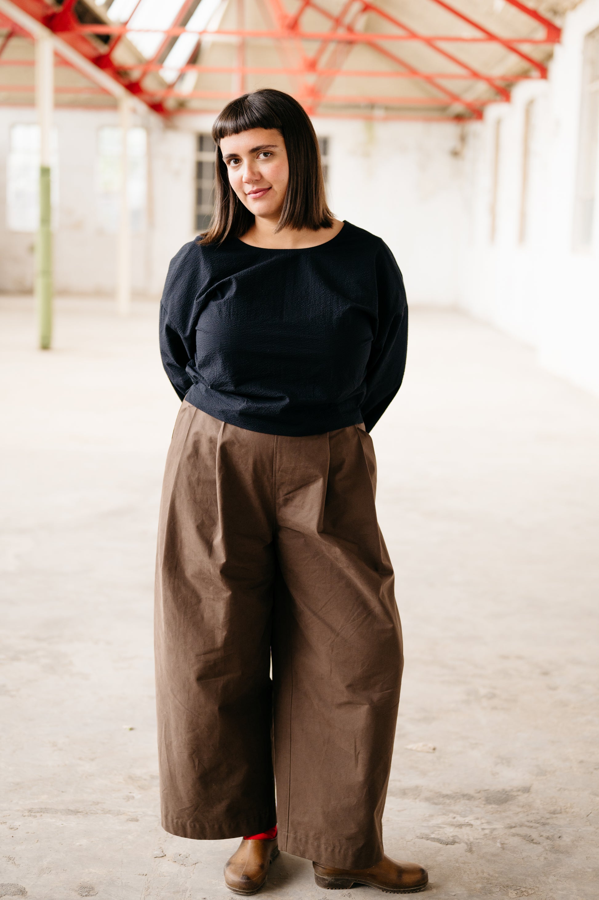 Person wearing a black top and brown pants in an indoor setting with red structural elements.