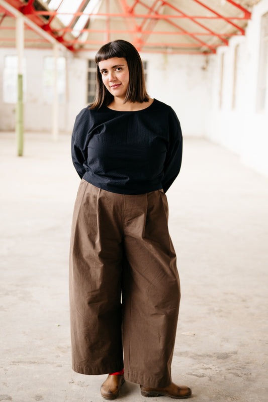 Person wearing a black top and brown pants in an indoor setting with red structural elements.