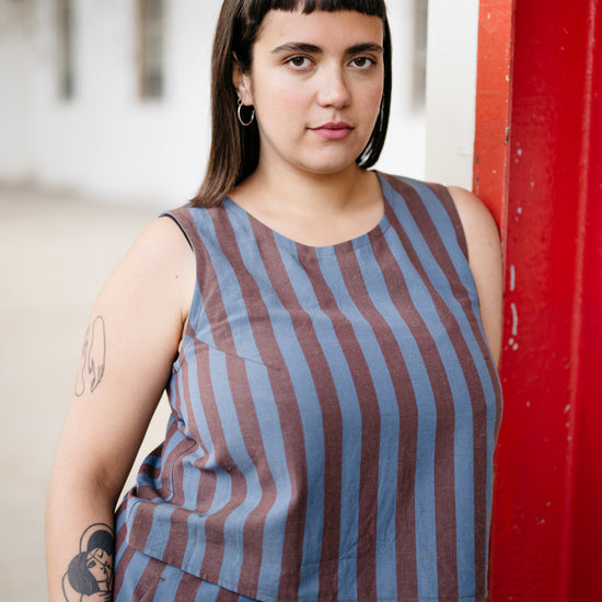 Woman wearing a striped sleeveless top and shorts against a red wall.