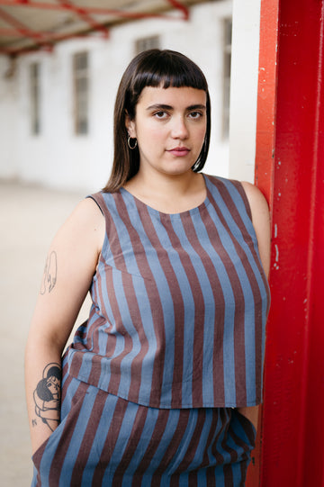 Woman wearing a striped sleeveless top and shorts against a red wall.