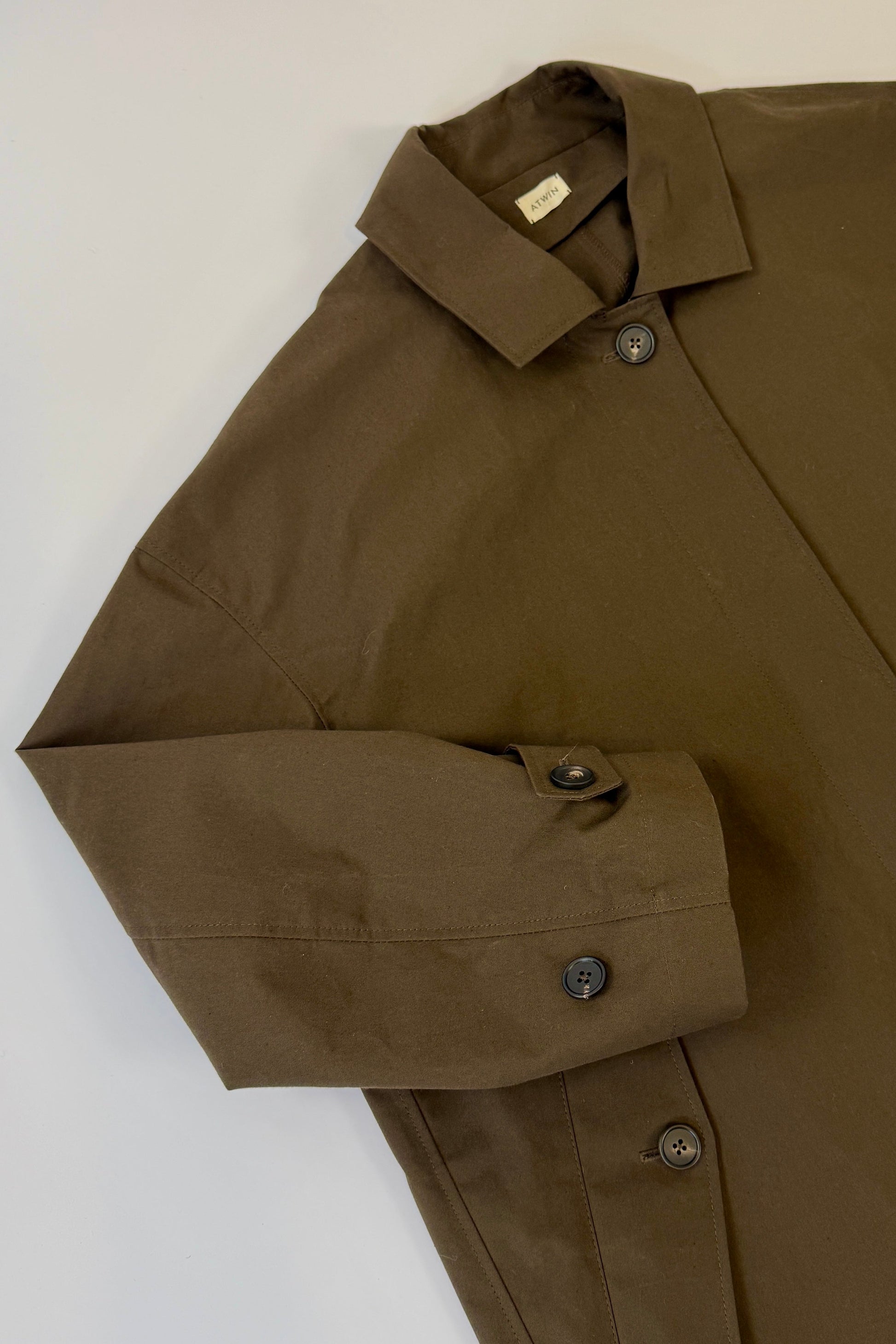 Brown wax rain mac jacket with button details on a white background
