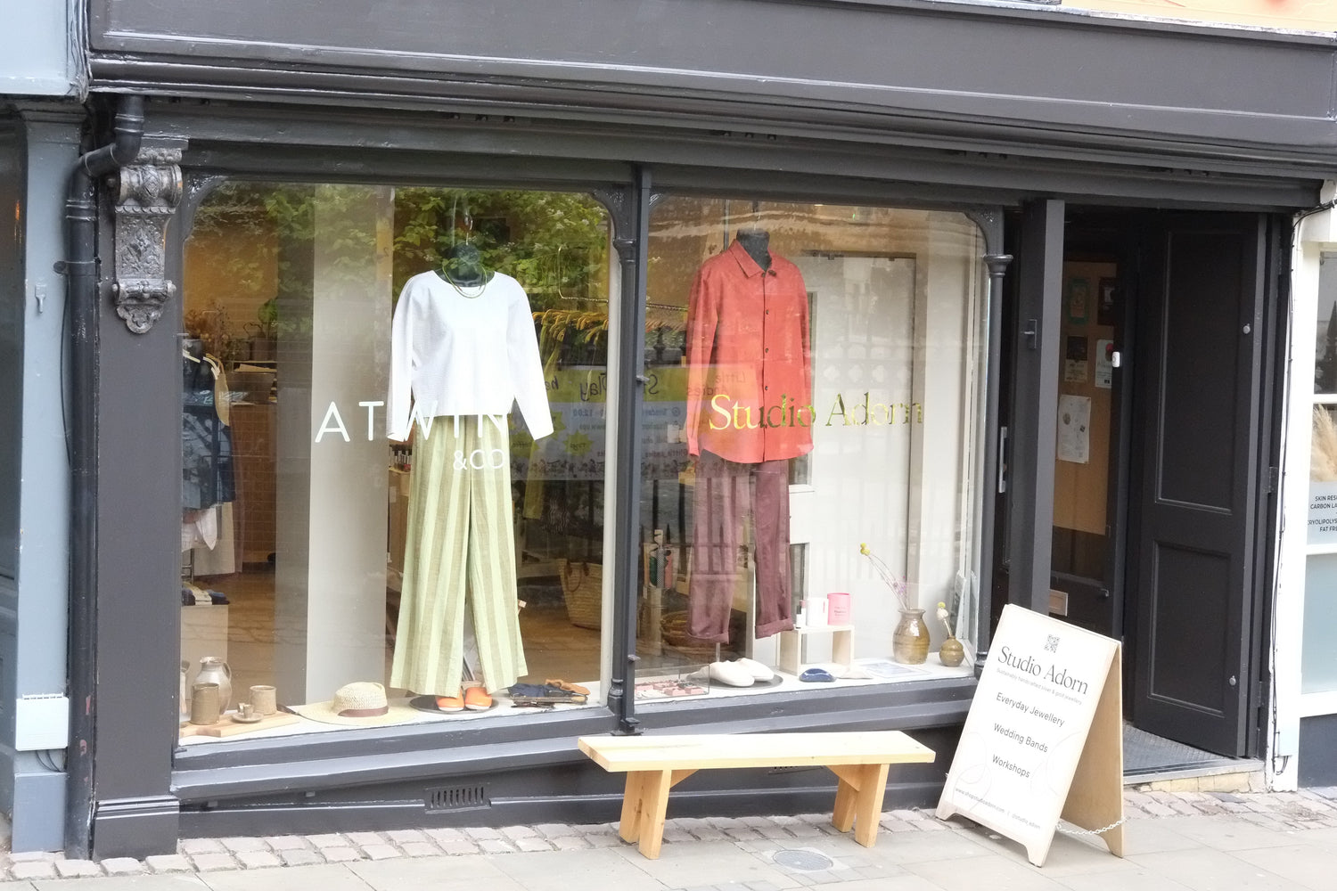 Storefront with a display of clothing and accessories, including a white top, green skirt, and red shirt.