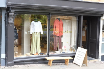 Storefront with a display of clothing and accessories, including a white top, green skirt, and red shirt.