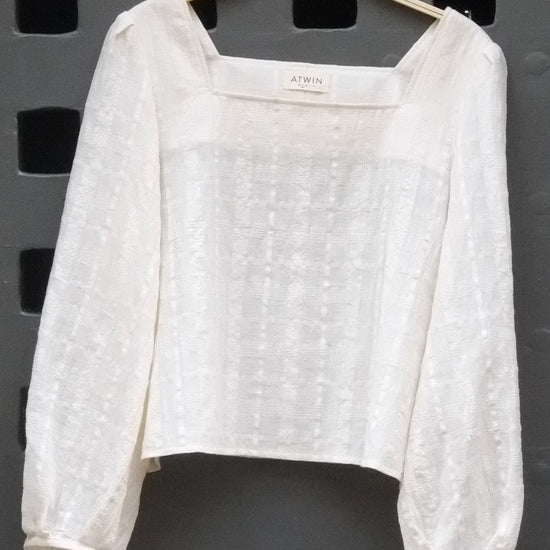 a cream coloured long sleeve top photographed hanging on. a grey door