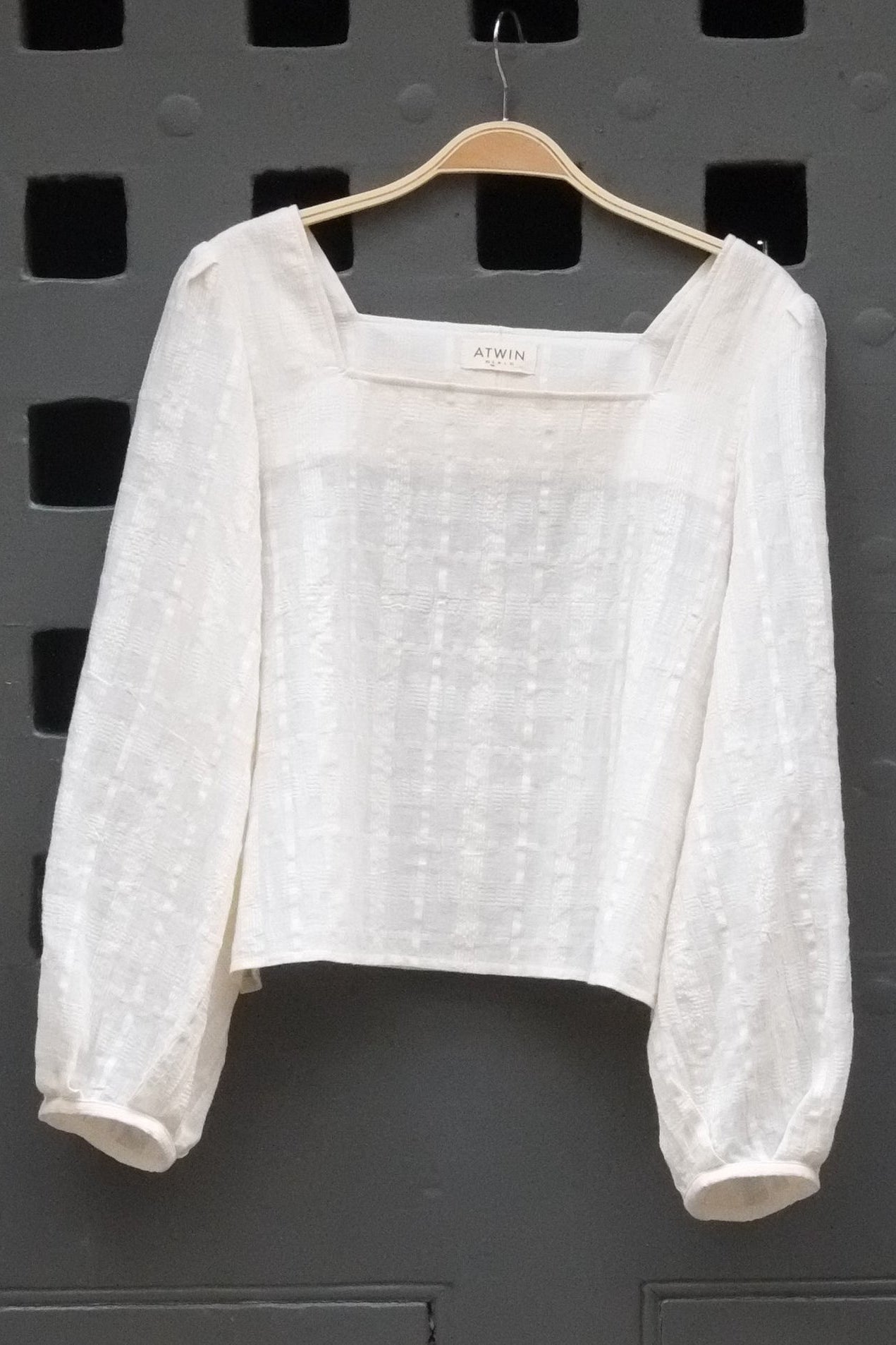 a cream coloured long sleeve top photographed hanging on. a grey door
